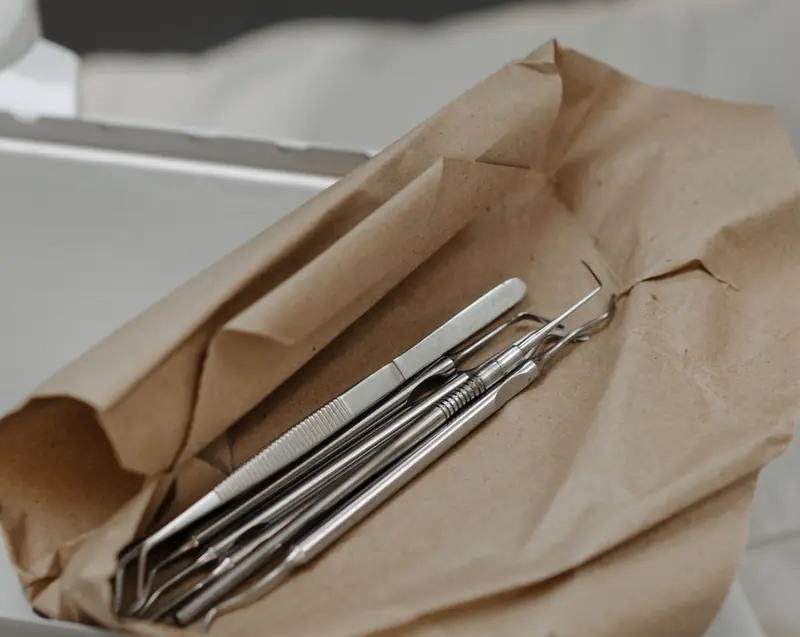 Steel dental instruments resting in an opened paper sterilisation pouch on a tray.