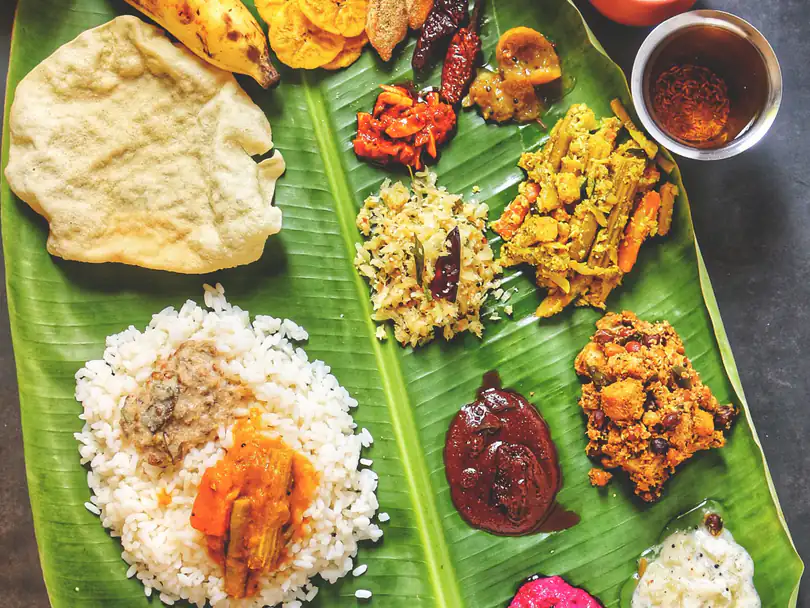 A full vegetarian meal on a banana leaf: rice with sambar, vegetables, pickle, appalam, banana chips and two bowls of payasam.