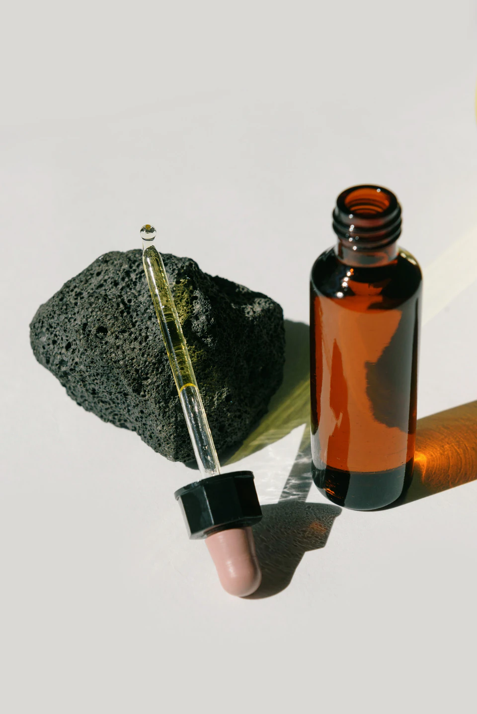 The open bottle beside its dropper and a piece of dark volcanic stone